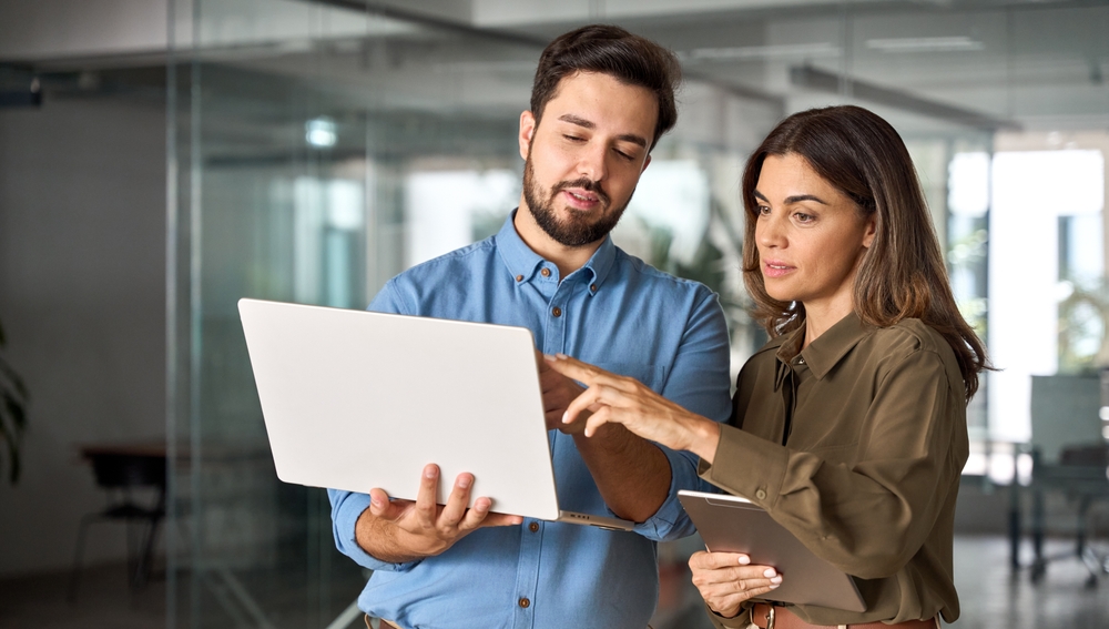 Two colleagues smiling while reviewing employee recognition programs data on a laptop in an open office